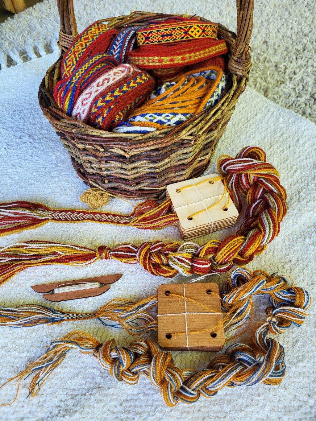 Värikkäitä puolivalmiita lautanauhoja pajukorissa ja sen edessä pöydällä